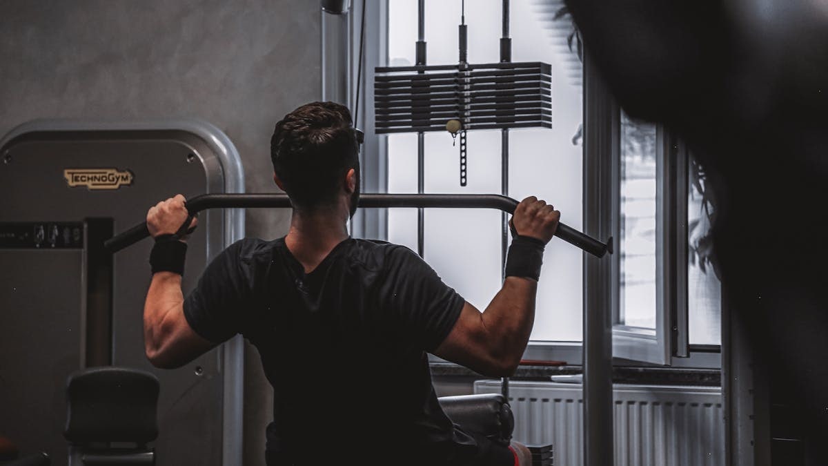 Back view of a man exercising with lat pulldown machine in the gym.